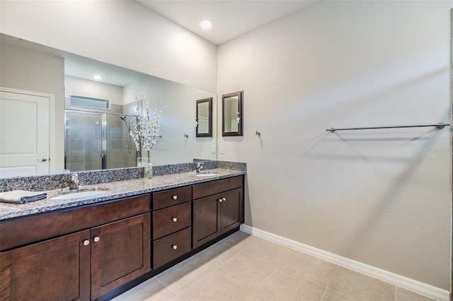 full bathroom with a stall shower, double vanity, a sink, and baseboards