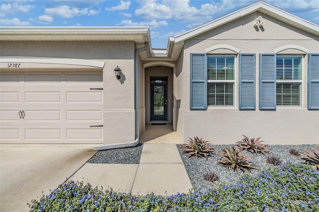 property entrance featuring concrete driveway, a garage, and stucco siding