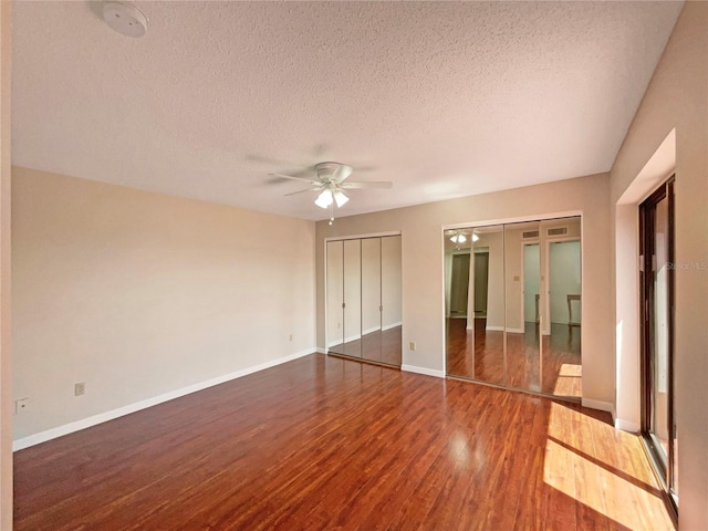 unfurnished bedroom with baseboards, ceiling fan, a textured ceiling, multiple closets, and wood finished floors