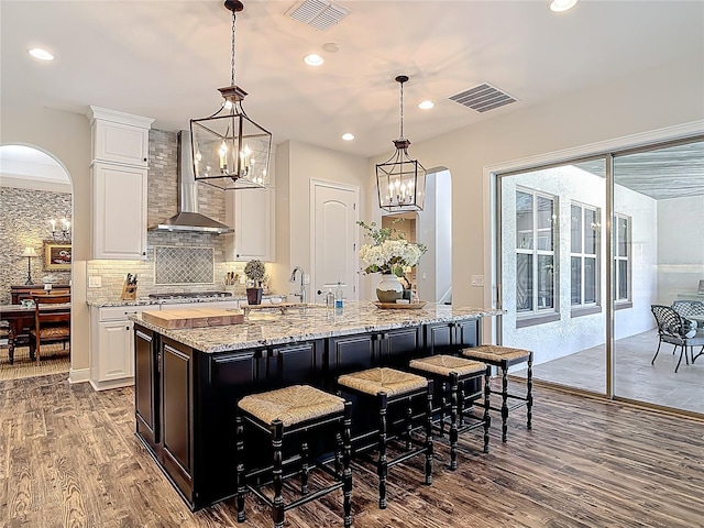 kitchen with tasteful backsplash, dark wood-style floors, white cabinets, visible vents, and wall chimney exhaust hood