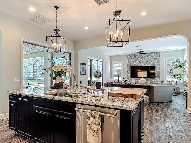kitchen featuring an island with sink, visible vents, dark cabinetry, arched walkways, and a sink