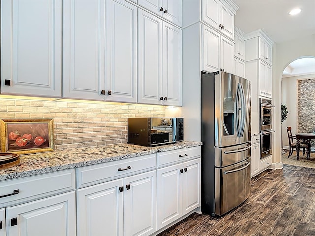 kitchen featuring tasteful backsplash, dark wood-style flooring, white cabinetry, appliances with stainless steel finishes, and arched walkways