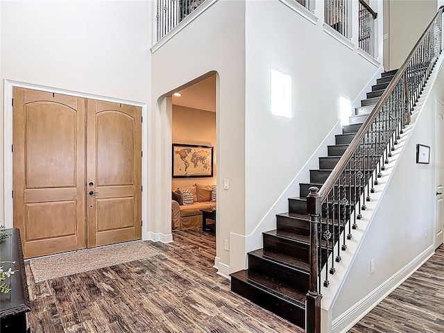 entryway with stairway, a towering ceiling, baseboards, and dark wood finished floors
