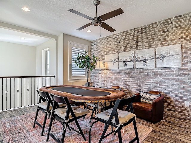 recreation room featuring a textured ceiling, a ceiling fan, recessed lighting, wood finished floors, and brick wall
