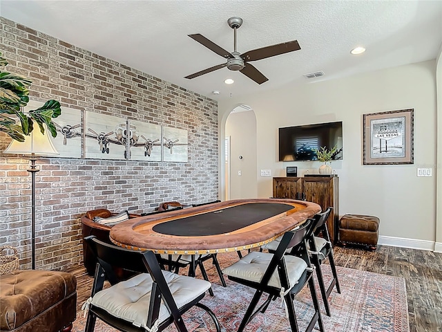 dining area with a ceiling fan, arched walkways, wood finished floors, and brick wall