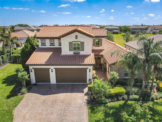 mediterranean / spanish-style home with a garage, stucco siding, a tile roof, and decorative driveway