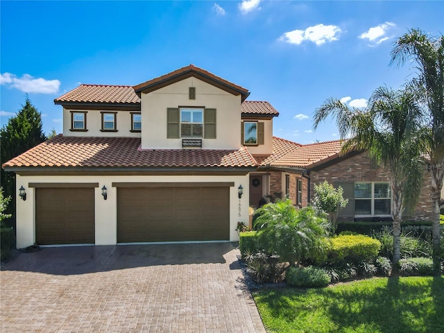 mediterranean / spanish-style home with stucco siding, decorative driveway, an attached garage, and a tile roof