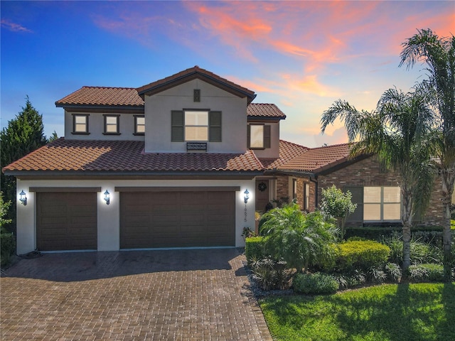 mediterranean / spanish-style home with an attached garage, a tiled roof, stucco siding, and decorative driveway