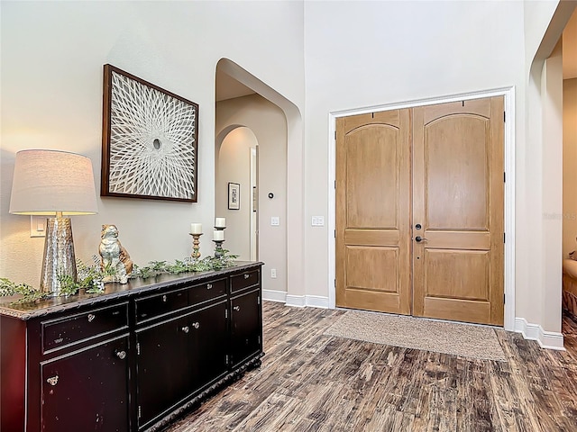entrance foyer with arched walkways, dark wood-style flooring, baseboards, and a high ceiling