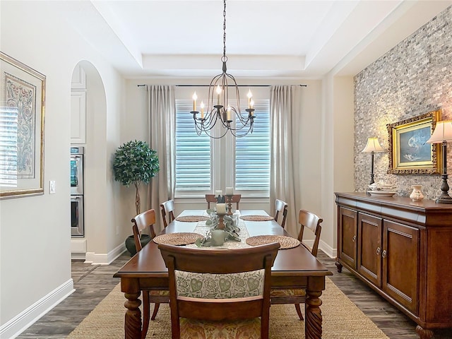 dining space with a notable chandelier, baseboards, dark wood-style floors, a raised ceiling, and arched walkways