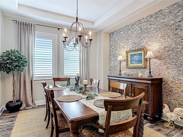dining area with a chandelier, a tray ceiling, baseboards, and dark wood finished floors