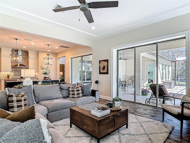 living room featuring visible vents, light wood-style flooring, arched walkways, and ceiling fan with notable chandelier
