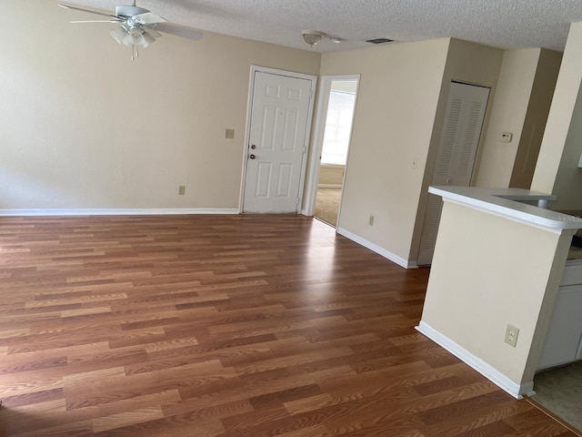 unfurnished living room featuring ceiling fan, visible vents, a textured ceiling, and wood finished floors