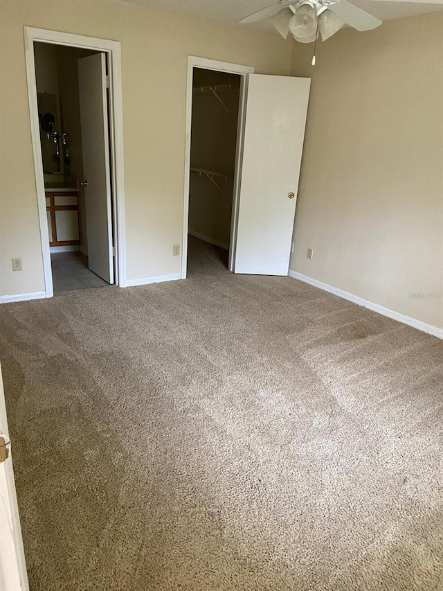 unfurnished bedroom featuring a walk in closet, carpet, a closet, and baseboards