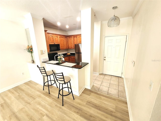2528 Robert Trent Jones Dr Unit 1617, Orlando, FL 32835 - kitchen featuring black microwave, freestanding refrigerator, brown cabinetry, a breakfast bar area, and light wood finished floors