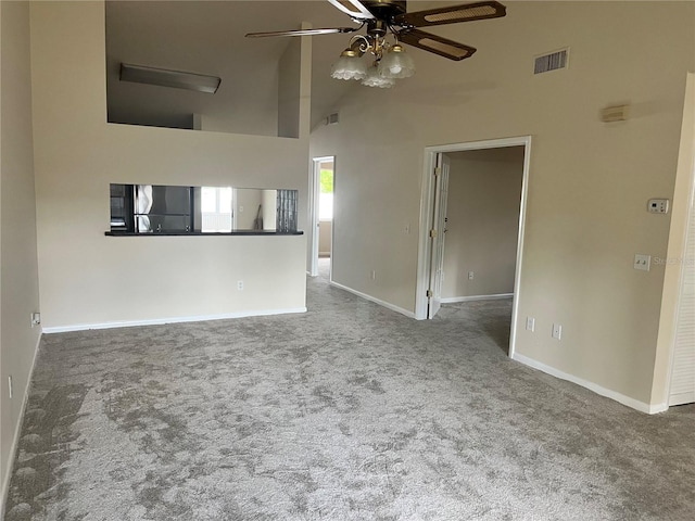 unfurnished living room with ceiling fan, a towering ceiling, visible vents, baseboards, and carpet