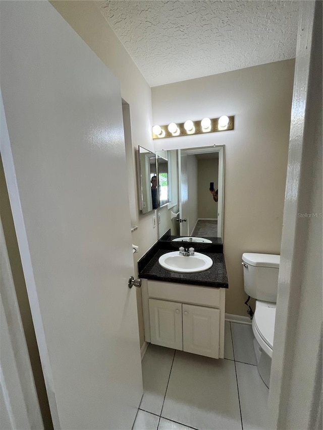 half bathroom with vanity, baseboards, tile patterned floors, and toilet