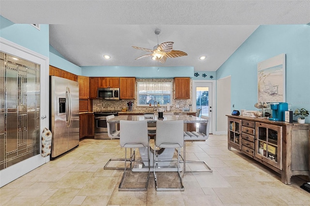 kitchen featuring tasteful backsplash, brown cabinets, vaulted ceiling, and stainless steel appliances
