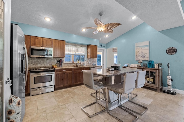 kitchen featuring stone counters, appliances with stainless steel finishes, backsplash, ceiling fan, and a sink