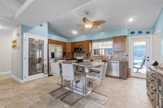 kitchen with brown cabinetry, a ceiling fan, stainless steel appliances, decorative backsplash, and a breakfast bar area