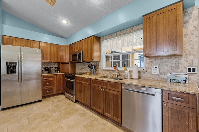 kitchen with backsplash, light stone countertops, brown cabinetry, stainless steel appliances, and a sink