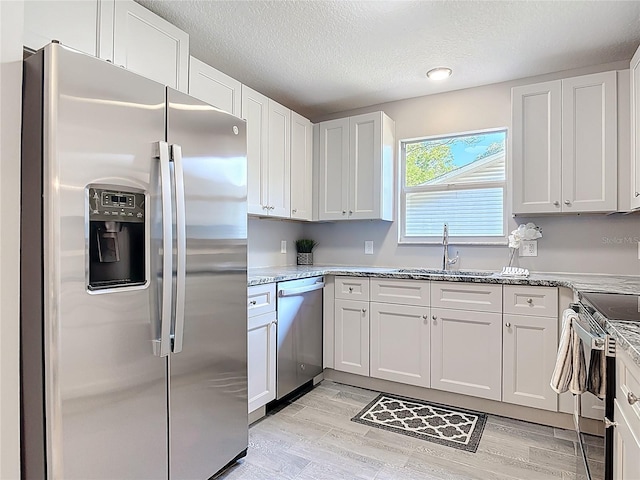 kitchen with a sink, a textured ceiling, appliances with stainless steel finishes, white cabinetry, and light stone countertops