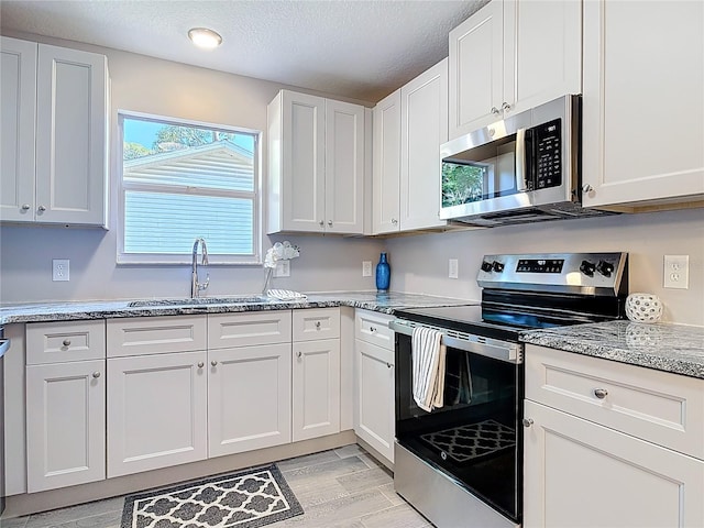kitchen featuring white cabinets, appliances with stainless steel finishes, light stone counters, and a sink