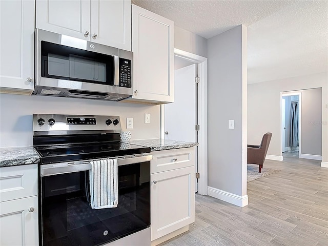 kitchen featuring appliances with stainless steel finishes, light stone counters, white cabinetry, and light wood-type flooring