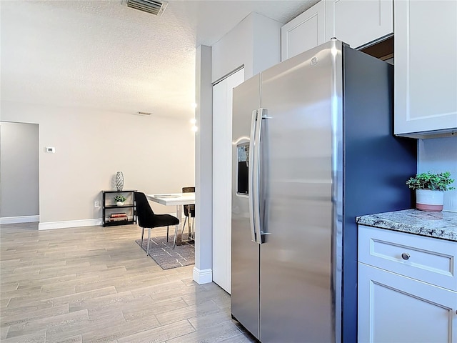 kitchen featuring visible vents, light stone countertops, baseboards, light wood-style flooring, and stainless steel refrigerator with ice dispenser
