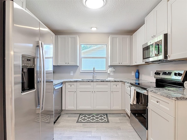 kitchen featuring a textured ceiling, a sink, white cabinetry, appliances with stainless steel finishes, and light stone countertops