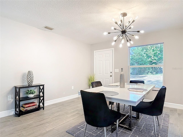 dining room with visible vents, a chandelier, light wood finished floors, and a textured ceiling