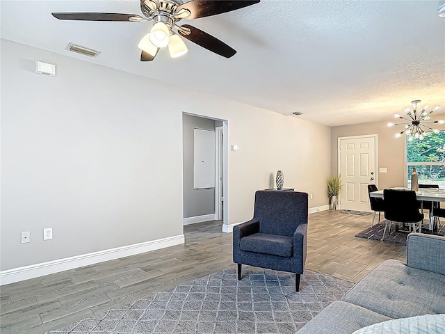 living room featuring a textured ceiling, visible vents, baseboards, ceiling fan with notable chandelier, and wood finished floors