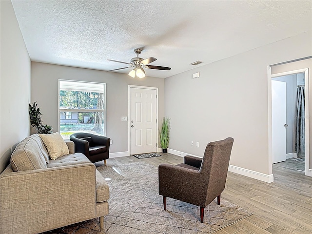 living area featuring visible vents, baseboards, light wood-style flooring, a textured ceiling, and ceiling fan