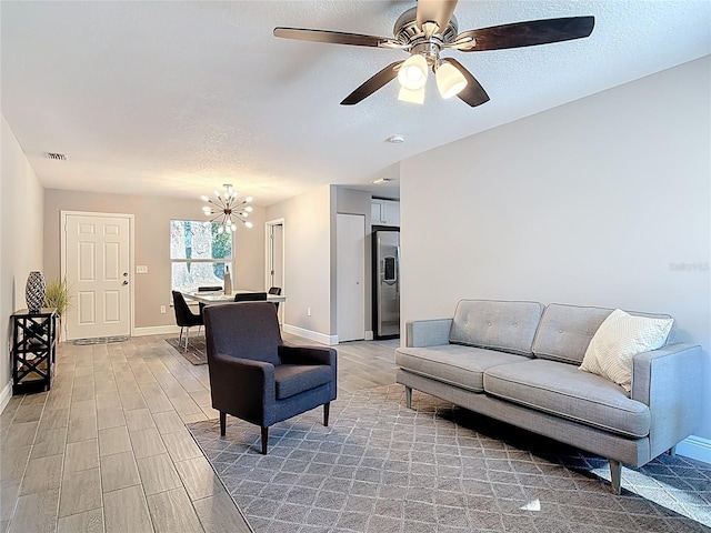 living area featuring light wood-style floors, a textured ceiling, baseboards, and ceiling fan with notable chandelier