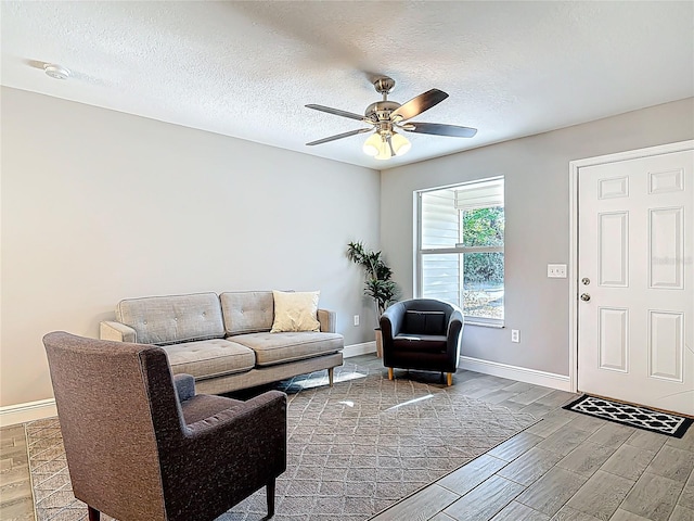 living area featuring ceiling fan, wood finish floors, a textured ceiling, and baseboards