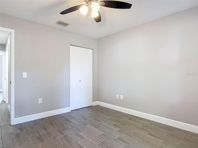 unfurnished bedroom with a textured ceiling, visible vents, baseboards, a ceiling fan, and wood finished floors