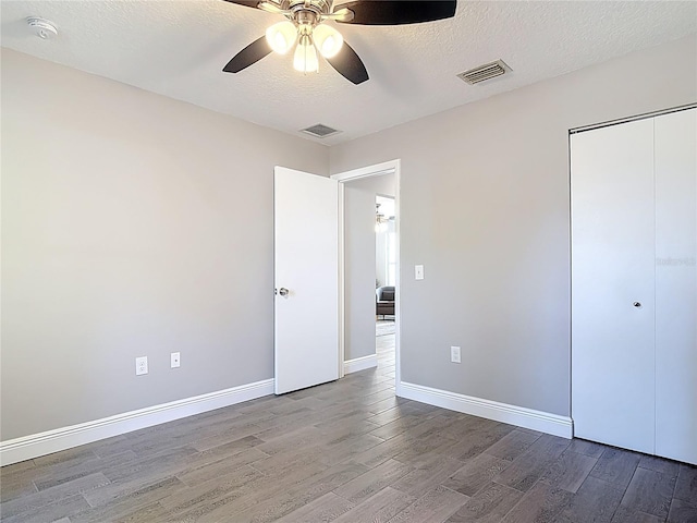 unfurnished bedroom with a textured ceiling, wood finished floors, visible vents, and a closet