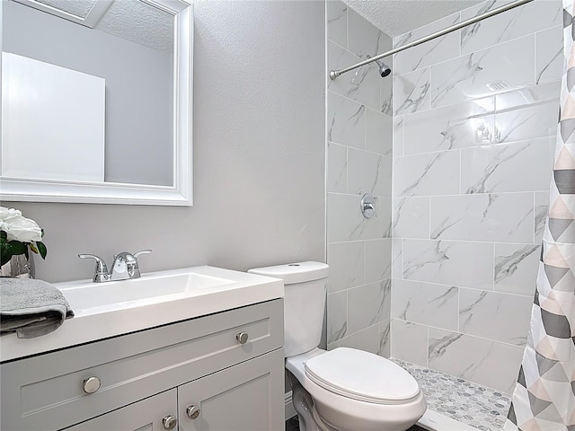 full bathroom featuring a tile shower, toilet, vanity, and a textured ceiling