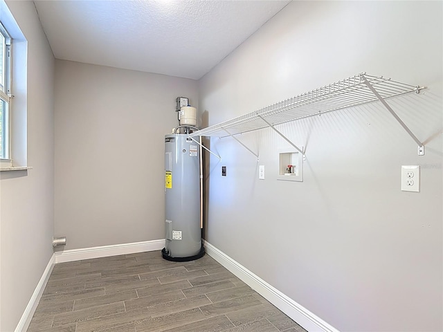 laundry room featuring electric water heater, baseboards, hookup for a washing machine, wood finished floors, and laundry area