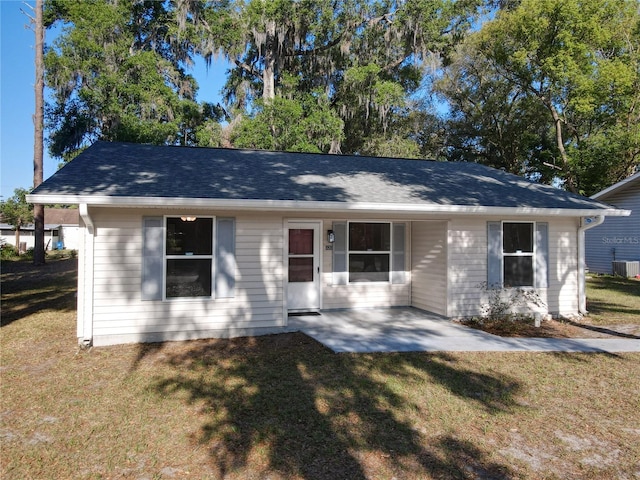 view of front facade with roof with shingles, a patio, and a front lawn