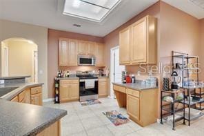 5005 Cape Hatteras Dr, Clermont, FL 34714 - kitchen with white microwave, stainless steel electric range oven, light brown cabinetry, and arched walkways