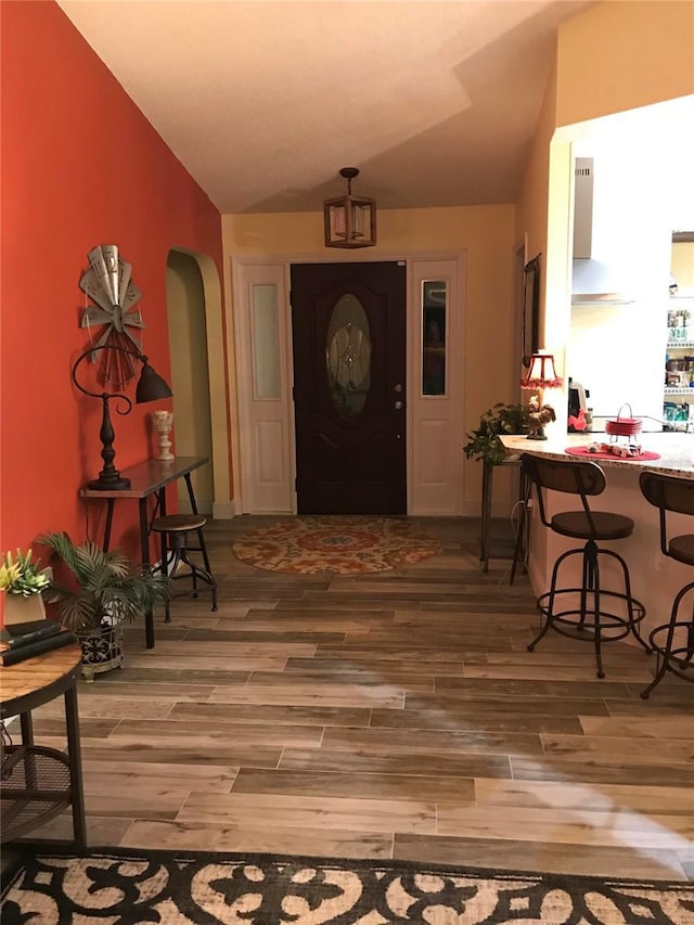 entryway with arched walkways, wood finished floors, and lofted ceiling