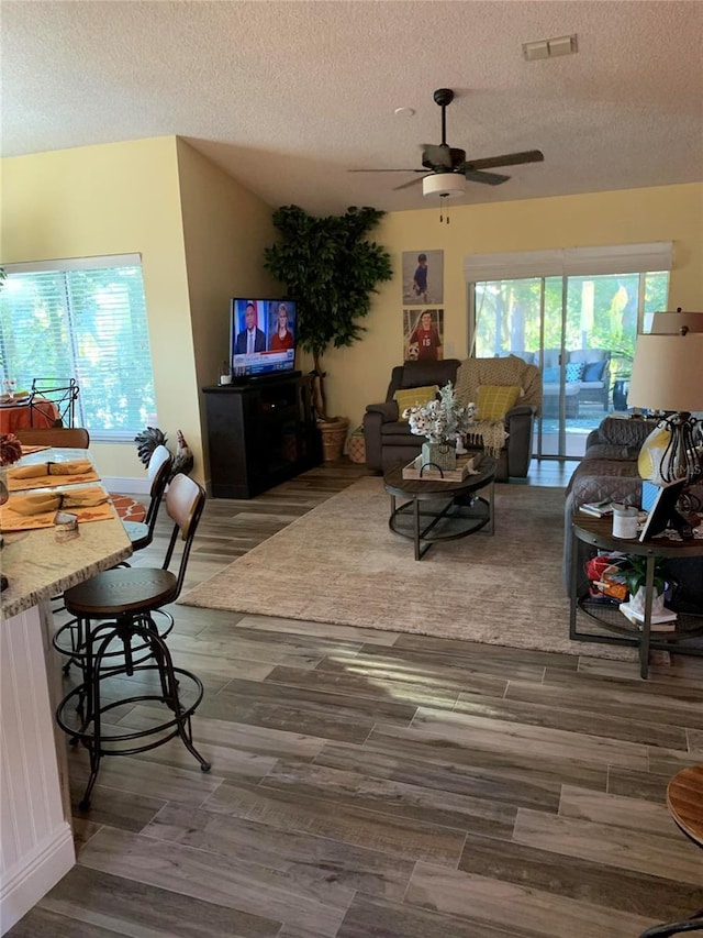 living area featuring visible vents, ceiling fan, wood finished floors, and a textured ceiling