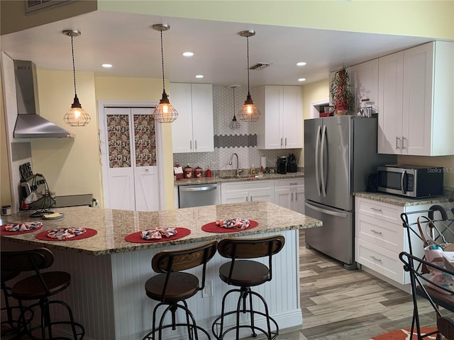kitchen featuring a breakfast bar area, appliances with stainless steel finishes, wall chimney exhaust hood, and visible vents