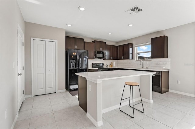 kitchen featuring dark brown cabinetry, a center island, backsplash, visible vents, and black appliances