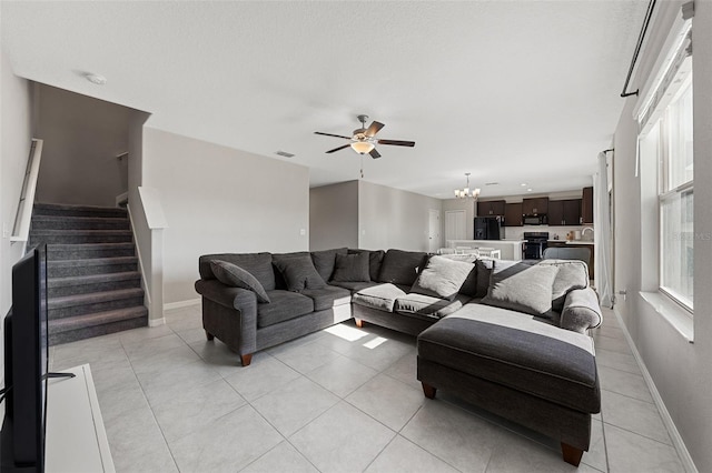 living room featuring ceiling fan with notable chandelier, baseboards, light tile patterned floors, visible vents, and stairway