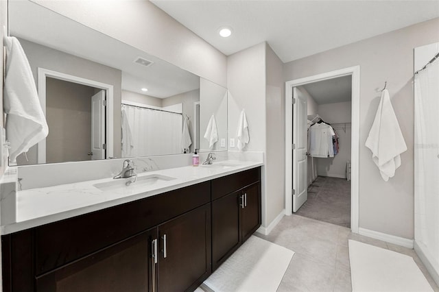 bathroom with visible vents, double vanity, baseboards, a spacious closet, and a sink