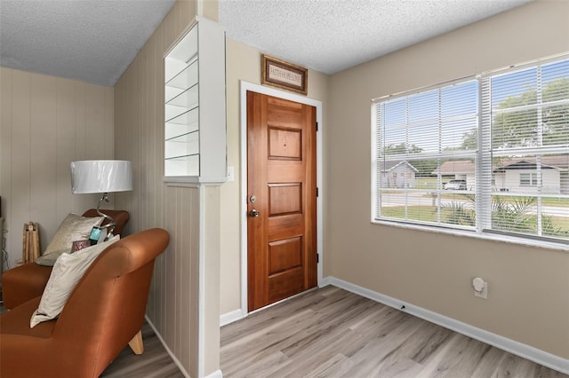 foyer entrance with light wood-style flooring, baseboards, and a textured ceiling