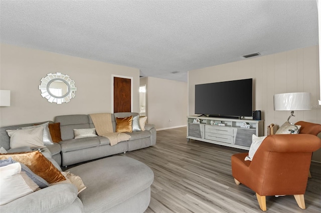 living area with visible vents, a textured ceiling, baseboards, and wood finished floors