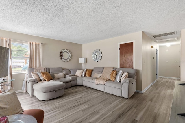 living room featuring a textured ceiling, light wood finished floors, baseboards, and visible vents